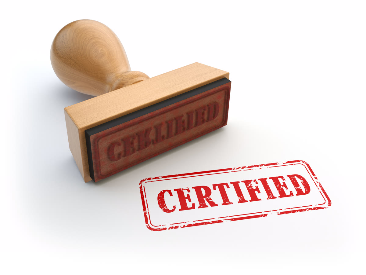 빨간 CERTIFIED 인영과 나무 고무인이 놓인 사진으로, 원본 서류에 공식 확인이 찍히는 인증 단계를 표현한 이미지